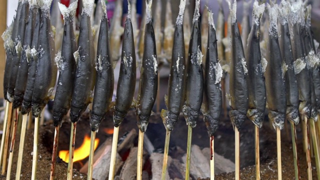 烤鱼放在炭棒上。小贩在市场街上做食物视频素材