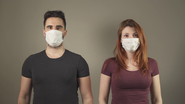 法国covid-19大流行病毒期间，一对戴着外科口罩的年轻夫妇站在演播室面对镜头。4K超高清。两个人。疾病预防。人际关系中的社会距离。视频下载