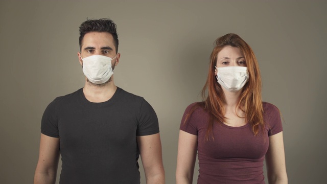 法国covid-19大流行病毒期间，一对戴着外科口罩的隔离年轻夫妇站在演播室里面对镜头。4K超高清。两个人。疾病预防。人际关系中的社会距离。视频下载
