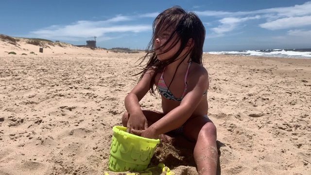 小女孩在沙滩上玩沙子，用沙子填满水桶视频素材