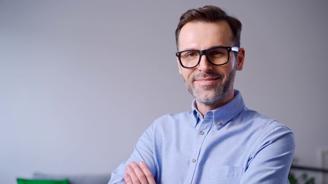 一个戴着眼镜的快乐男人在家里对着照相机微笑的特写视频下载