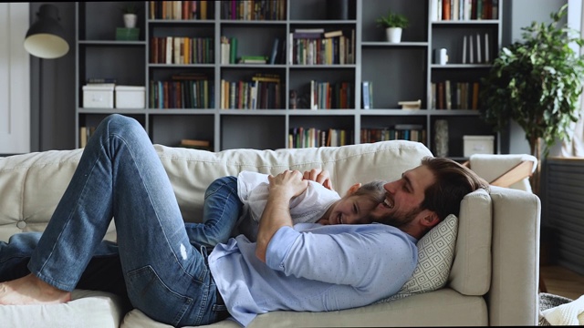 快乐可爱的女儿和爸爸在沙发上搔痒视频素材