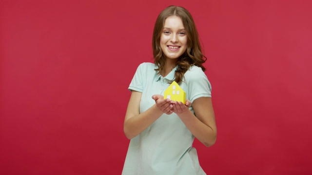 迷人的活泼美丽的年轻女子在马球t恤拿着纸房子和微笑的相机视频下载