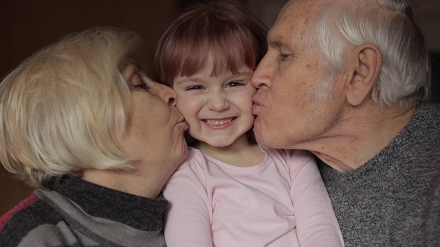爷爷和奶奶在家里亲吻他们的小孙女的脸颊视频下载