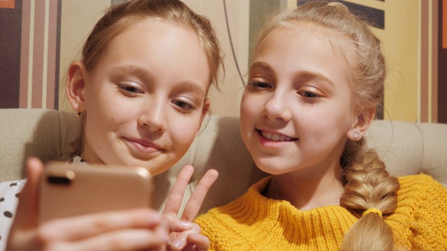 两名少女在手机自拍中显示胜利标志。少女微笑和摆姿势的手机照片的智能手机。视频下载