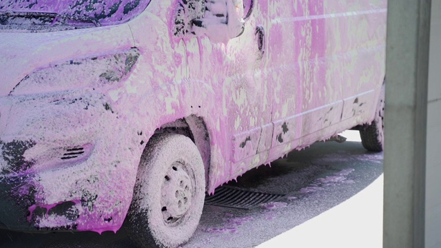 汽车被泡沫覆盖在洗车。洗车工人把泡沫涂在汽车上视频素材