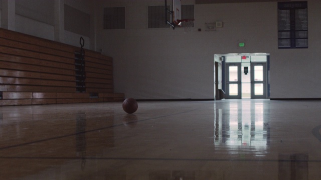 一个低角度的篮球坐在一个空的学校体育馆。视频素材
