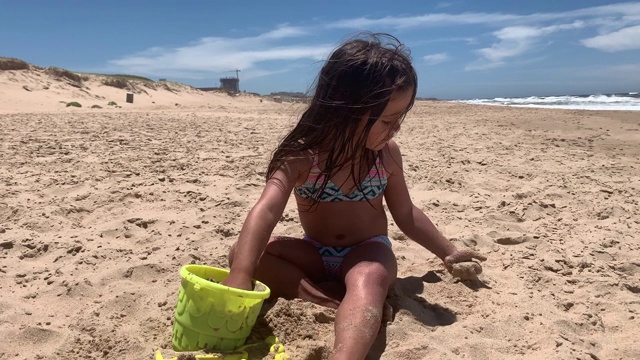 小女孩在沙滩上玩沙子和水桶视频素材