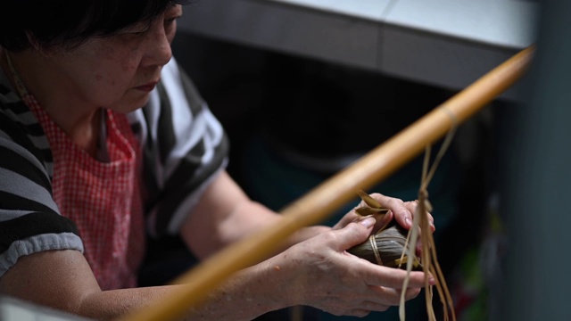 一位年长的亚洲华人妇女在她的厨房里准备粽子，把配料包好，为端午节做准备视频素材