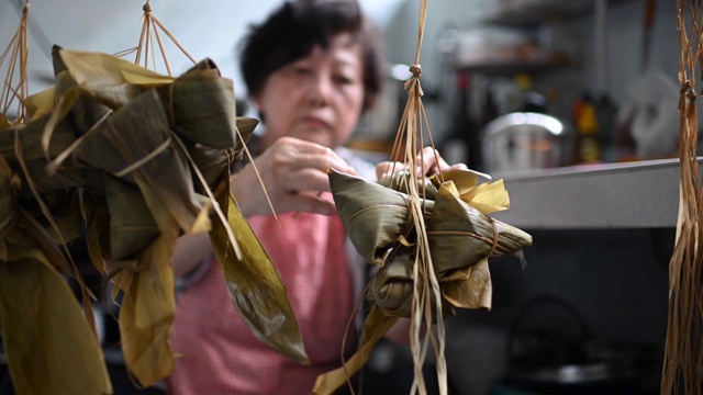 一位年长的亚洲华人妇女在她的厨房里准备粽子，把配料包好，为端午节做准备视频下载