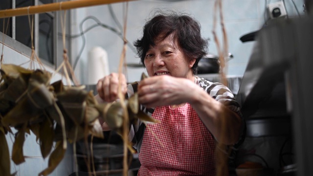 一位年长的亚洲华人妇女在她的厨房里准备粽子，把配料包好，为端午节做准备视频下载
