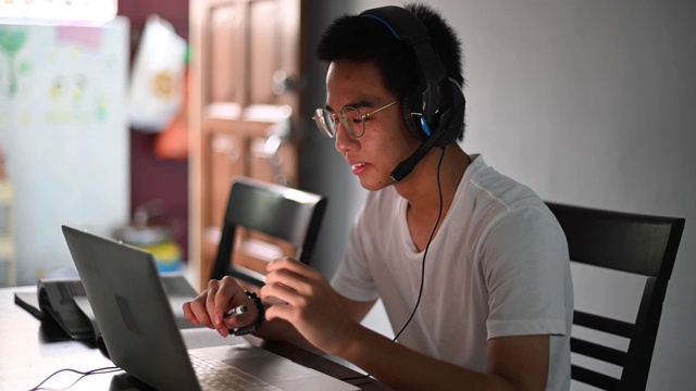一名亚裔中国少年一边在厨房餐桌上做作业，一边通过网络软件与所有同学在线聊天视频下载