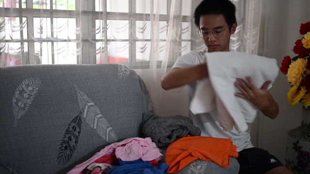 一个亚裔中国少年帮他的母亲叠干净的衣服视频素材