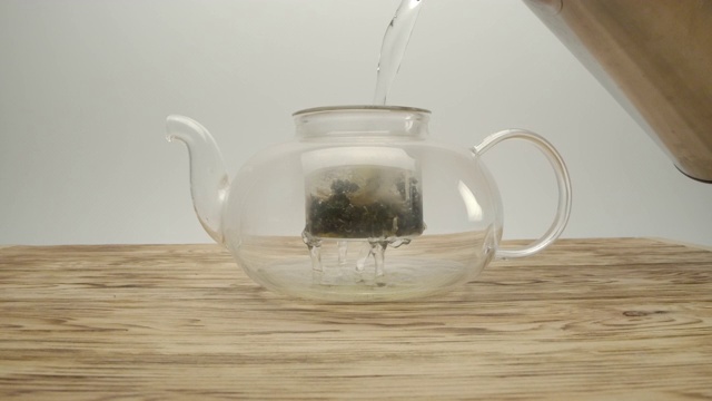 将开水从水壶中倒入木桌上茶壶中的白茶中视频下载