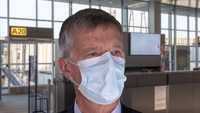 肖像中的年长男子戴着防Covid-19口罩，深呼吸，让口罩在机场背景下进出视频素材