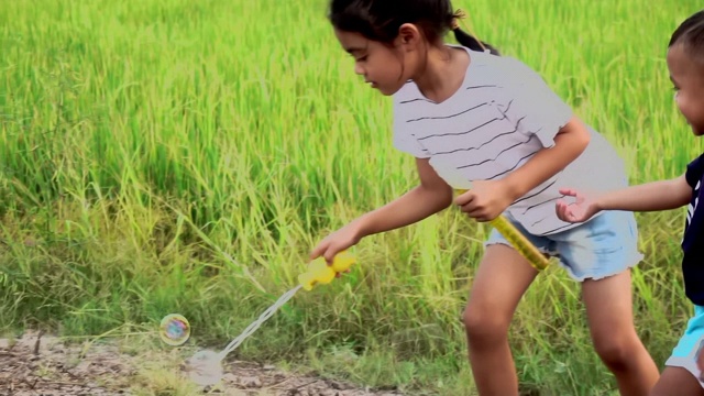 亚洲的孩子们笑着，在夏天的绿色稻田里吹泡泡，慢动作视频素材