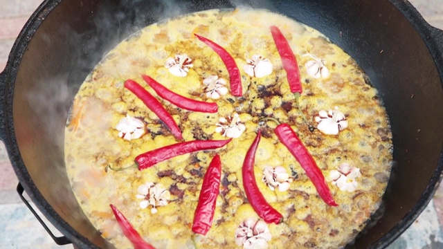 乌兹别克民族菜肴肉饭，肉饭，plov，米饭和肉放在大锅里。煮至沸腾，在大锅中烧红辣椒和整个大蒜视频素材