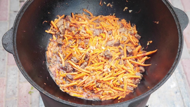 烹制乌兹别克国菜肉饭，肉饭，胡萝卜与肉放在大锅里。烹饪过程中，明火。在着火的釜中烹饪。用撇油器慢慢搅拌。加入小切的胡萝卜视频素材