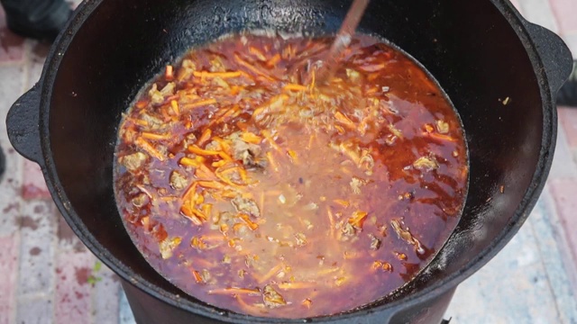 烹制乌兹别克国菜肉饭，肉饭，胡萝卜与肉放在大锅里。加水，煮制过程，明火。在着火的釜中烹饪。用撇油器慢慢搅拌。添加香料视频素材