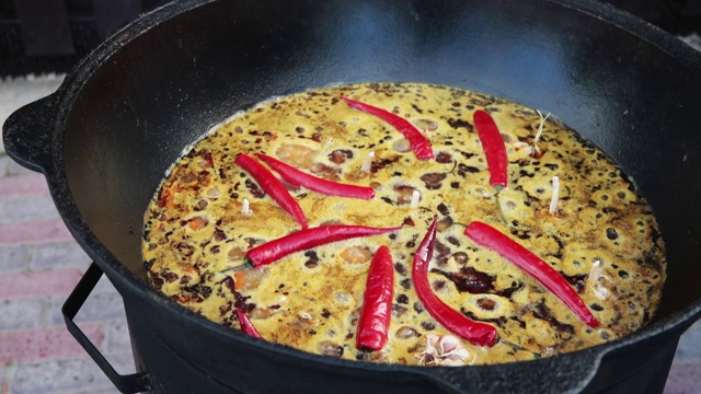 乌兹别克民族菜肴肉饭，肉饭，plov，米饭和肉放在大锅里。煮至沸腾，在大锅中烧红辣椒和整个大蒜视频素材