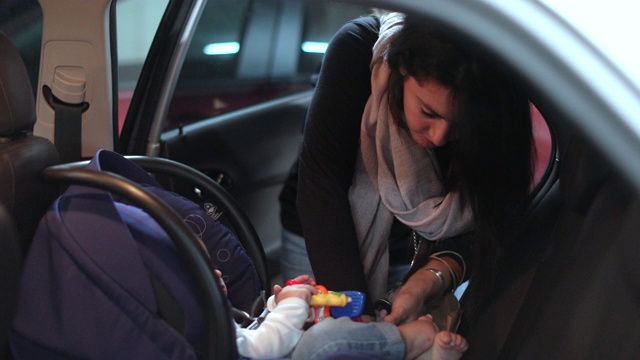 母亲把她的婴儿牢牢地安置在汽车的安全座椅上视频素材