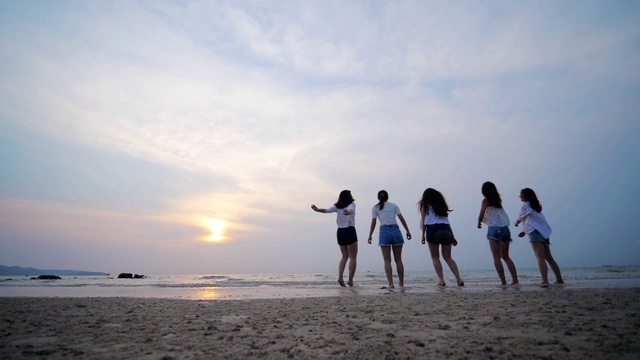 一群朋友欢天喜地，在沙滩上跳跃着落日的剪影视频素材