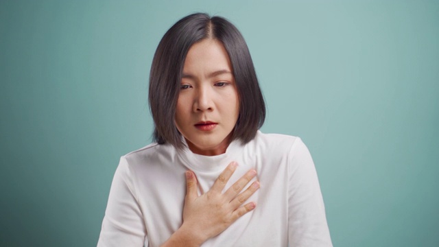 一名亚洲妇女病了，气喘吁吁，孤立地站在蓝色背景上。卫生保健的概念。4 k的视频。视频下载