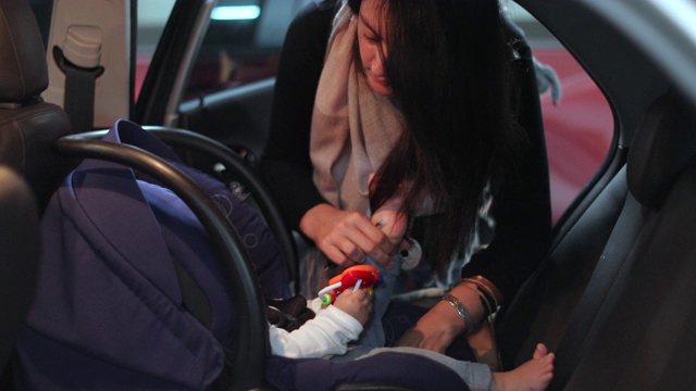 母亲把她的婴儿牢牢地安置在汽车的安全座椅上视频素材