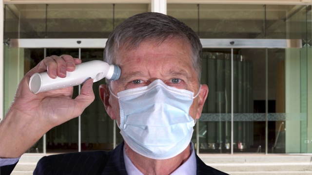 一位戴口罩的长者在办公室门口量体温，检查病毒视频素材