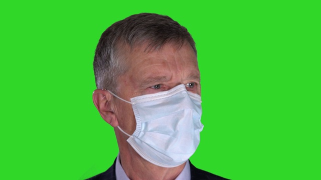 肖像中的资深男子戴着抗击新冠肺炎的口罩，深呼吸，让口罩在绿屏上来回移动视频素材