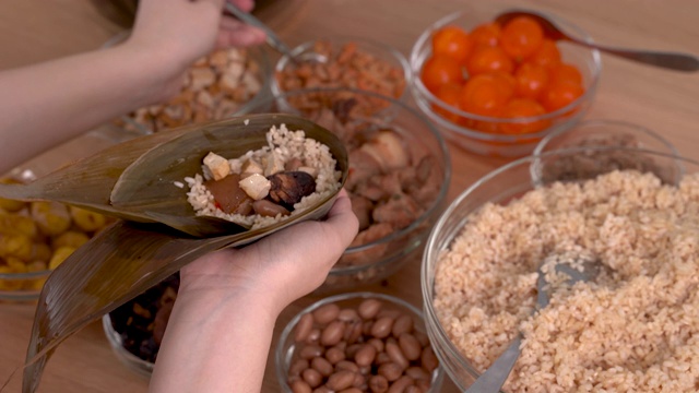 包粽子——家庭准备，在家里的木桌上一起包一束粽子，庆祝端午节。视频素材