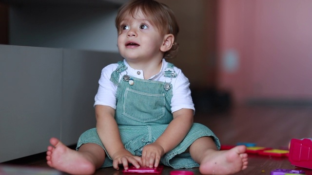 一岁的婴儿坐在家里的地板上玩玩具，蹒跚学步的婴儿呆在家里独自玩视频素材