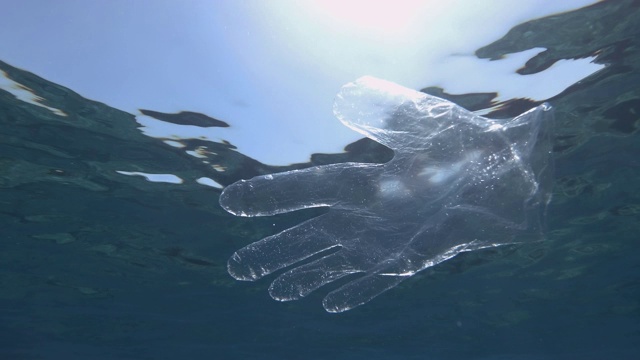 塑料污染，废弃的塑料手套在阳光下慢慢漂浮在蓝色的水面下。透明塑料手套漂浮在欧洲地中海。慢动作视频下载