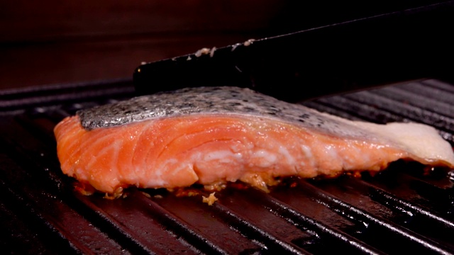 厨师用黑色抹刀将一片鲑鱼片放在烤架上视频素材