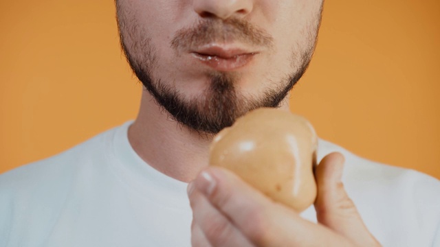 特写雄嘴吃苹果。一个穿着白色运动衫，长着鬃毛的男人。适当营养的概念。橙色简单的背景视频素材