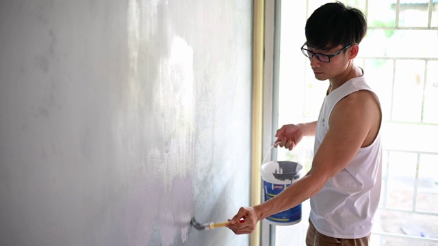 亚裔华人正在粉刷房子客厅的墙壁视频素材