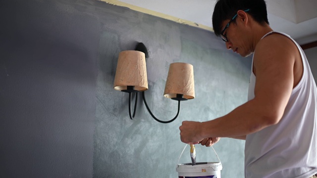 亚裔华人正在粉刷房子客厅的墙壁视频素材