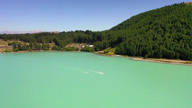 空中倾斜拍摄的人在绿松石湖上的水上滑板对天空，无人机从森林向后飞行在晴朗的一天-特卡波湖，新西兰视频下载