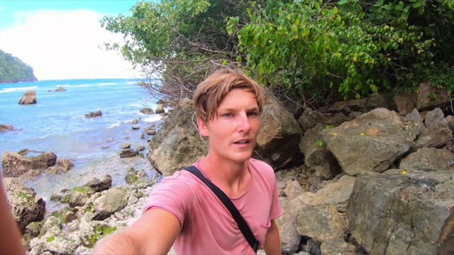 慢镜头平移拍摄的年轻男子站在海滩岩石- Wakatobi摄政，印度尼西亚视频下载