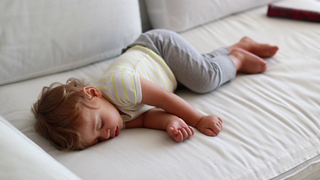 小婴儿在家里的沙发上打盹。可爱的蹒跚学步的婴儿懒洋洋地睡在沙发上视频素材