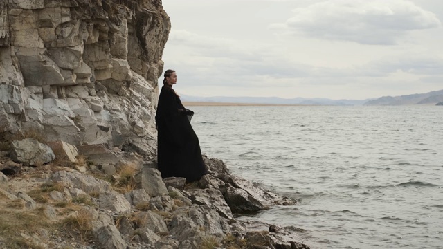 一个白人女孩站在湖岸的岩石下，穿着黑色的民族服装视频素材