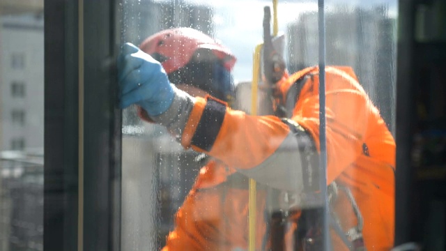 工业攀岩者穿着橙色的连体衣在慢镜头中清洗窗户。清洗窗户上的灰尘和污垢视频下载