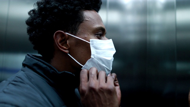 一名非洲黑人男子戴着冠状病毒口罩走进电梯，走出电梯视频下载