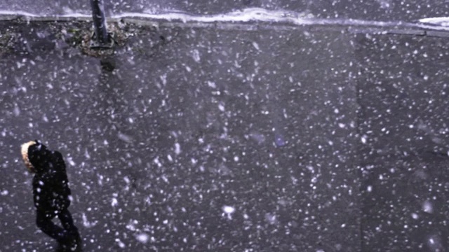 一个人走在飘落的雪下，上面的风景。冬天的街道视频素材