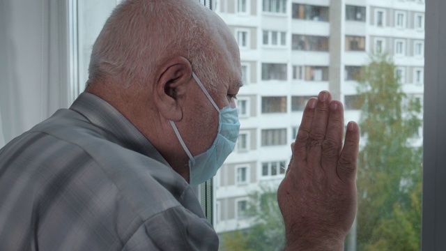 一位戴着医用防护口罩的老人在隔离期间望向窗外视频下载