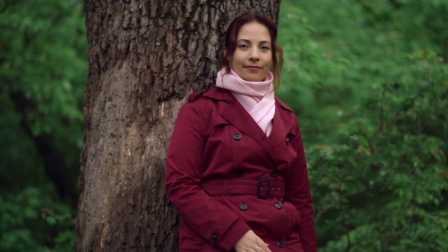年轻漂亮的女人的肖像在红色夹克站在树在春天的森林视频下载