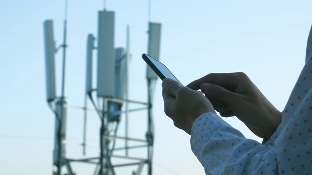 男子手持手机使用5G通信基站塔为背景视频素材