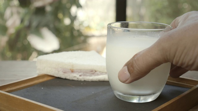 在一扇开着的窗户后面的棕色木桌上放着一杯白牛奶视频素材