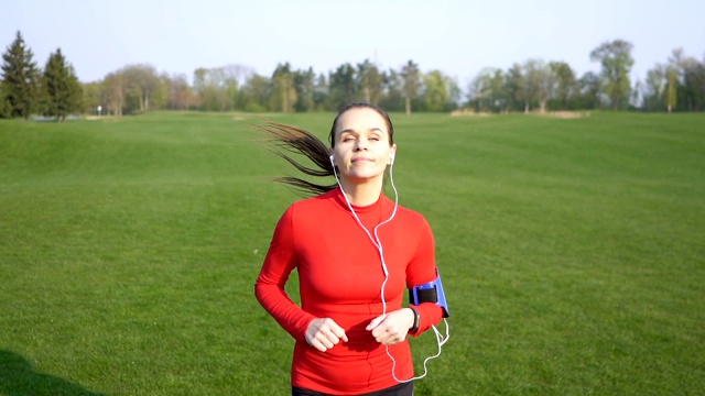 成年女子跑步者在绿地上奔跑。慢镜头，脸部特写视频素材