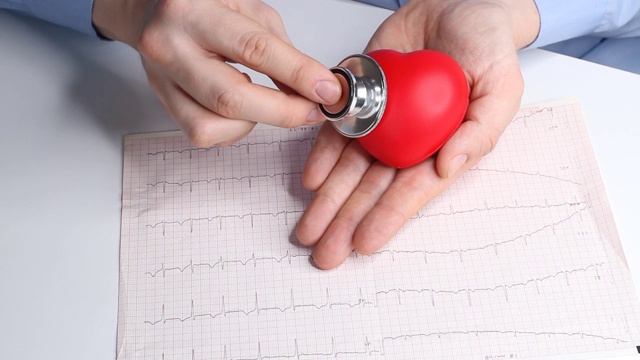 心脏病专家医生检查一个玩具红心的心率。耳内窥镜，听诊器和心电图。医疗保健和早期诊断的概念。视频素材